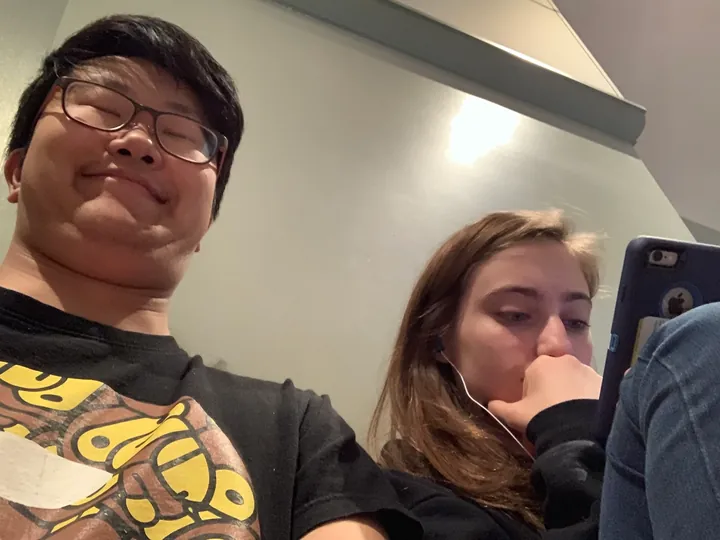 Daniel grinning at the camera while Hannah works on her phone beside him