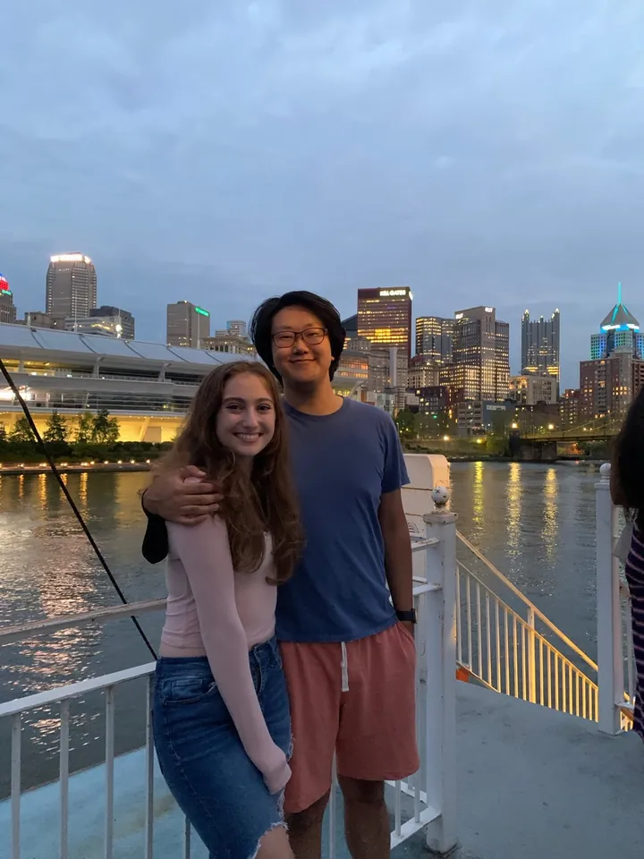 Hannah and Daniel at the rail, the city lit up across the water at dusk